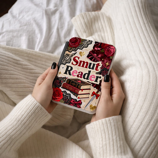 Hand holding Kindle Case with 'Smut Reader' design, surrounded by white fabric.